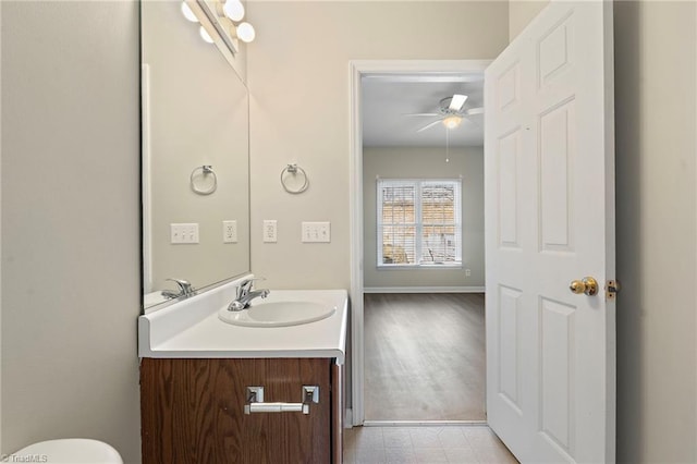 bathroom featuring baseboards, toilet, vanity, and a ceiling fan