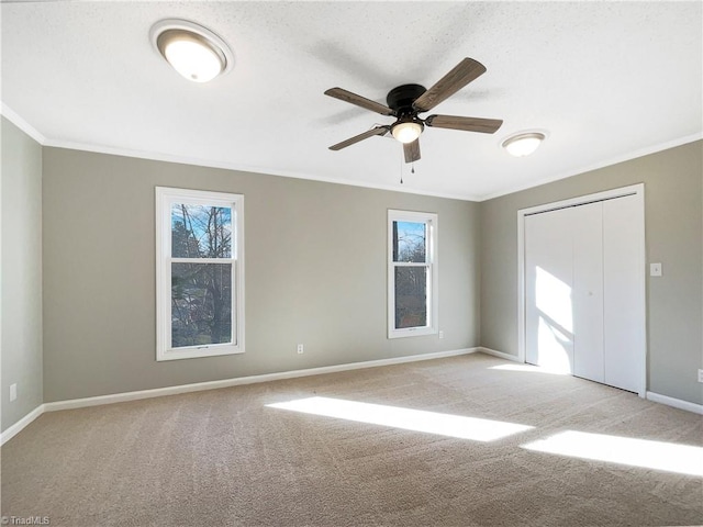 spare room featuring light carpet, ornamental molding, ceiling fan, and a wealth of natural light