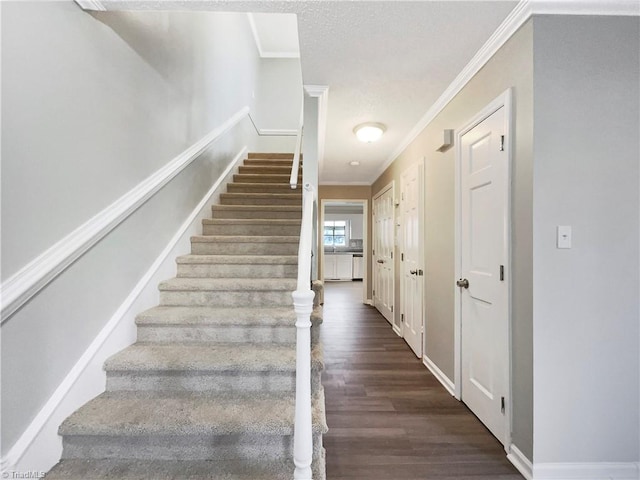 staircase featuring a textured ceiling, crown molding, and dark wood-type flooring