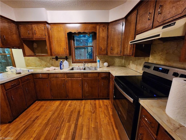 kitchen featuring light wood-type flooring, backsplash, a textured ceiling, stainless steel electric stove, and sink