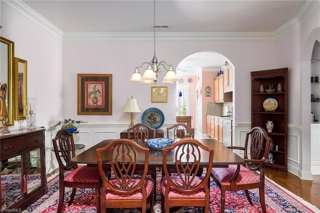 129 Turnbuckle Ct, Clemmons, NC 27012 - dining room featuring ornamental molding, arched walkways, wood finished floors, a chandelier, and wainscoting