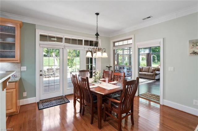 dining area featuring a wealth of natural light, ornamental molding, wood-type flooring, and a chandelier