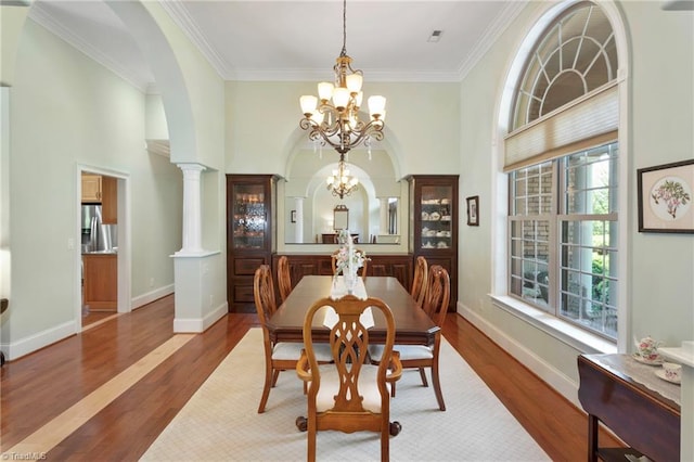 dining space with crown molding, dark wood-type flooring, ornate columns, and a notable chandelier