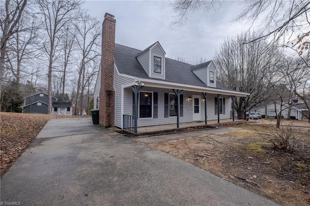 cape cod-style house featuring aphalt driveway, covered porch, and a chimney
