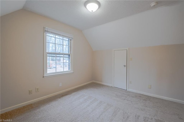 additional living space with vaulted ceiling, light carpet, and a textured ceiling