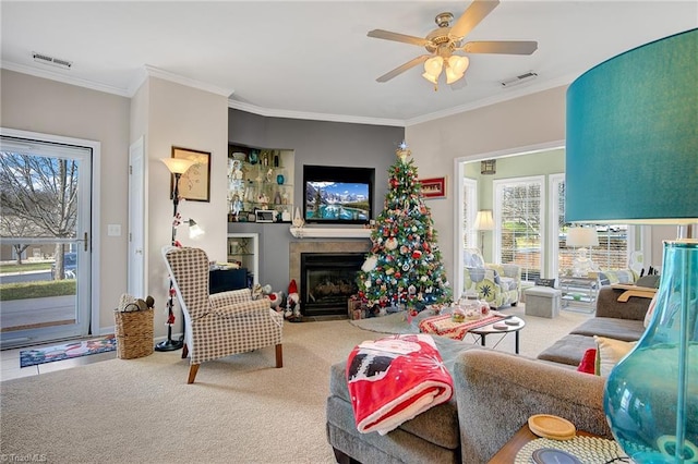 living room featuring a tiled fireplace, ceiling fan, carpet floors, and ornamental molding