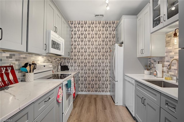 kitchen featuring sink, light stone counters, light hardwood / wood-style flooring, white appliances, and decorative backsplash