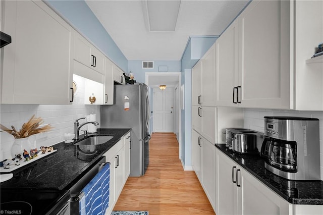 kitchen with white cabinets, dark stone counters, sink, and light hardwood / wood-style flooring