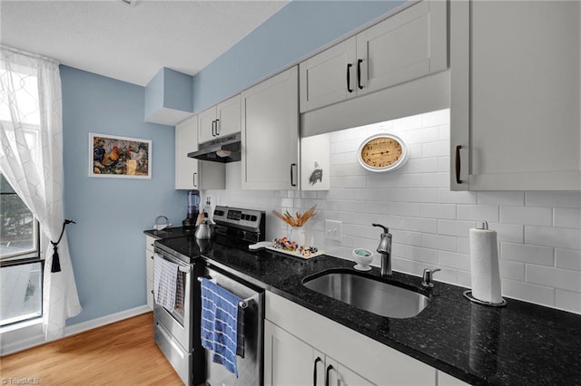 kitchen featuring light hardwood / wood-style floors, stainless steel appliances, dark stone counters, sink, and white cabinetry