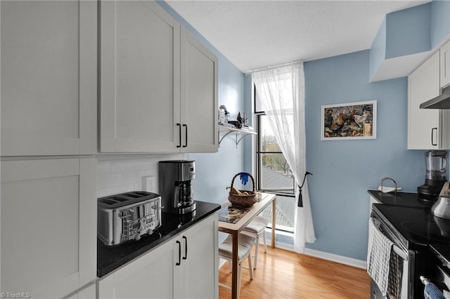 kitchen featuring stainless steel electric range, dark stone counters, white cabinets, decorative backsplash, and light hardwood / wood-style flooring