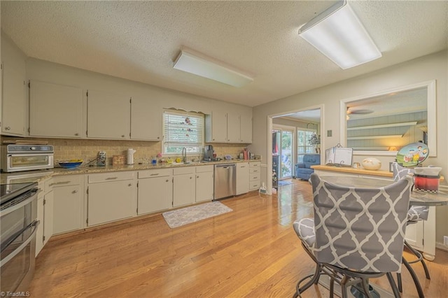 2205 Sedgemont Dr, Winston-Salem, NC 27103 - kitchen featuring light wood-type flooring, stainless steel appliances, a textured ceiling, tasteful backsplash, and white cabinetry