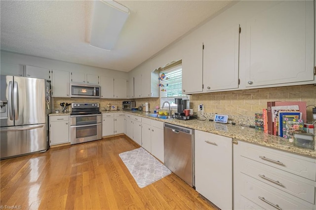 2205 Sedgemont Dr, Winston-Salem, NC 27103 - kitchen with stainless steel appliances, light wood-style floors, tasteful backsplash, light stone counters, and white cabinetry