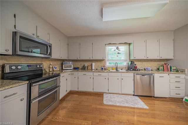 2205 Sedgemont Dr, Winston-Salem, NC 27103 - kitchen featuring stainless steel appliances, a textured ceiling, light wood finished floors, white cabinets, and decorative backsplash