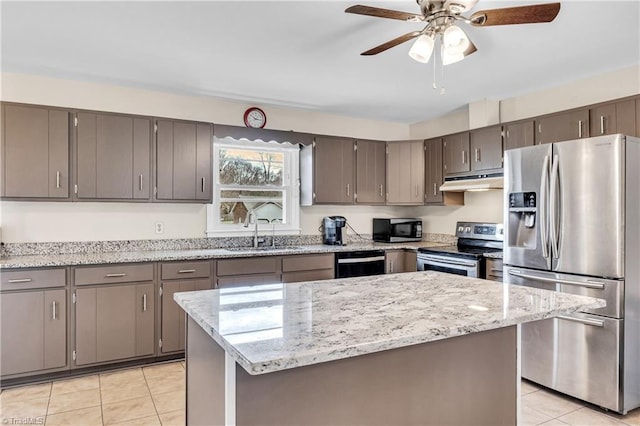 kitchen with under cabinet range hood, light tile patterned floors, light stone counters, stainless steel appliances, and a sink