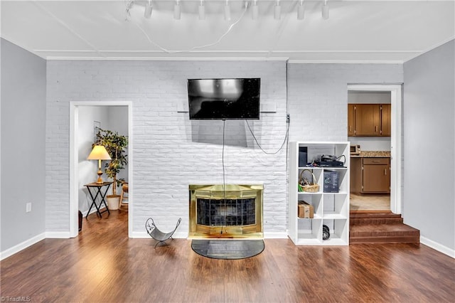 living room featuring a brick fireplace, brick wall, baseboards, and wood finished floors