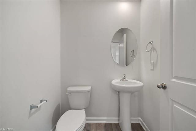 half bathroom with toilet, baseboards, a sink, and wood finished floors