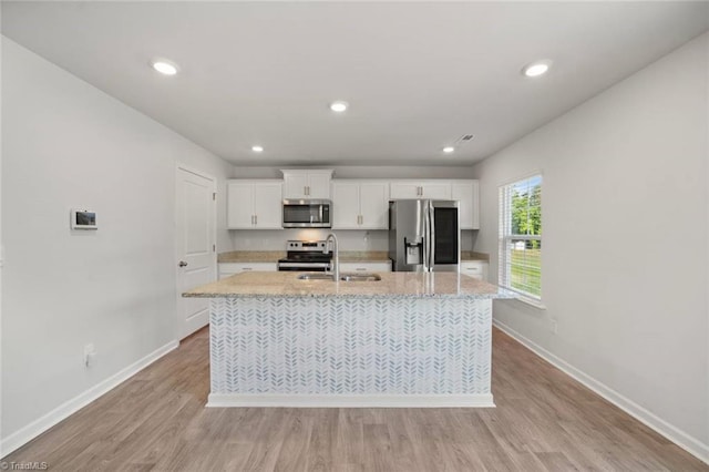 kitchen featuring a sink, stainless steel appliances, a kitchen island with sink, white cabinets, and baseboards