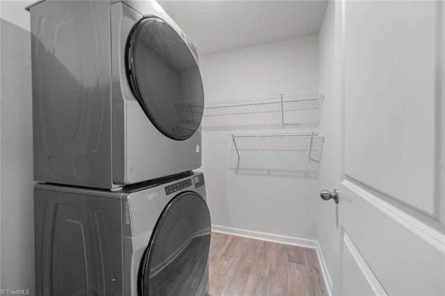 washroom featuring laundry area, stacked washing maching and dryer, wood finished floors, and baseboards