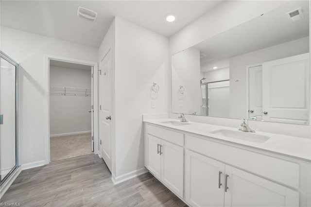 full bathroom with a stall shower, baseboards, double vanity, and a sink