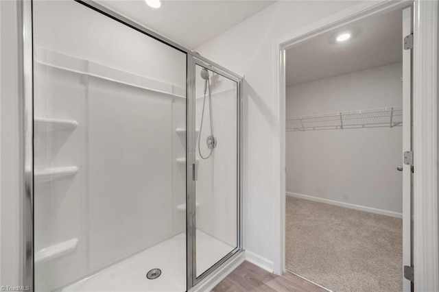 bathroom featuring a walk in closet, recessed lighting, baseboards, a shower stall, and wood finished floors