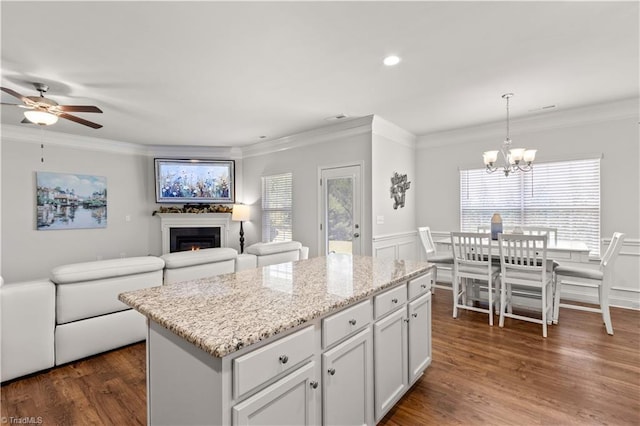 kitchen with white cabinets, ceiling fan with notable chandelier, ornamental molding, decorative light fixtures, and a kitchen island