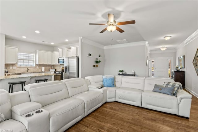 living room with ceiling fan, sink, ornamental molding, and dark wood-type flooring