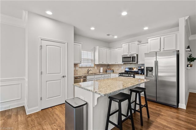 kitchen featuring white cabinets, light stone counters, appliances with stainless steel finishes, a kitchen island, and a kitchen bar