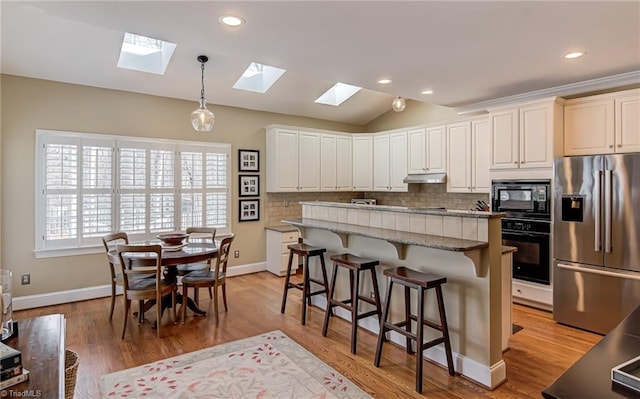 kitchen with black appliances, tasteful backsplash, vaulted ceiling with skylight, and under cabinet range hood