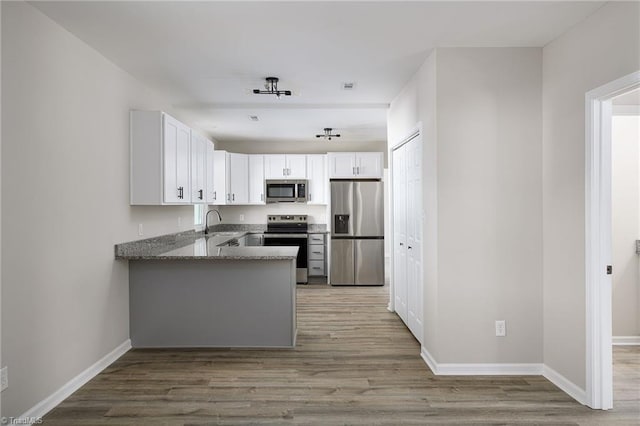 kitchen with light hardwood / wood-style flooring, stone counters, stainless steel appliances, white cabinets, and kitchen peninsula