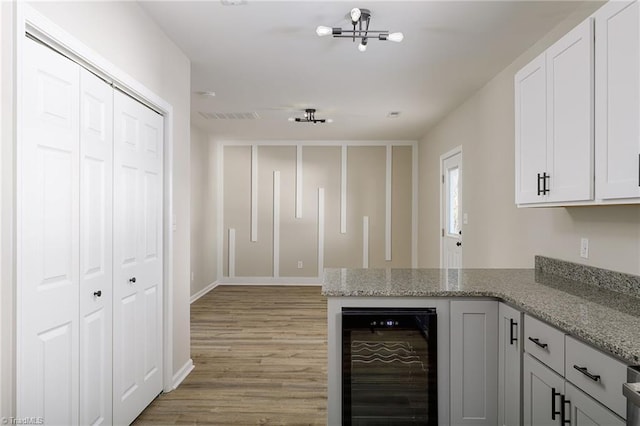 kitchen featuring light hardwood / wood-style flooring, white cabinetry, light stone counters, beverage cooler, and a chandelier