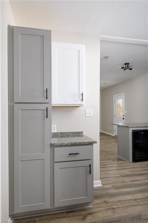 interior space with wine cooler, gray cabinets, hardwood / wood-style floors, and light stone counters