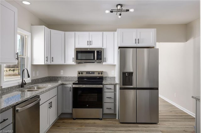 kitchen with appliances with stainless steel finishes, white cabinetry, sink, light stone counters, and light hardwood / wood-style flooring