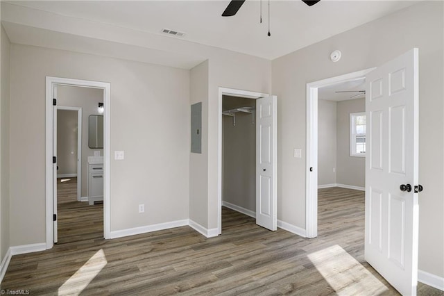 unfurnished bedroom with ceiling fan, electric panel, light hardwood / wood-style floors, a walk in closet, and a closet