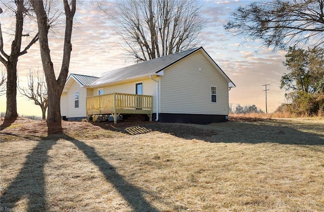 property exterior at dusk featuring a lawn and a deck