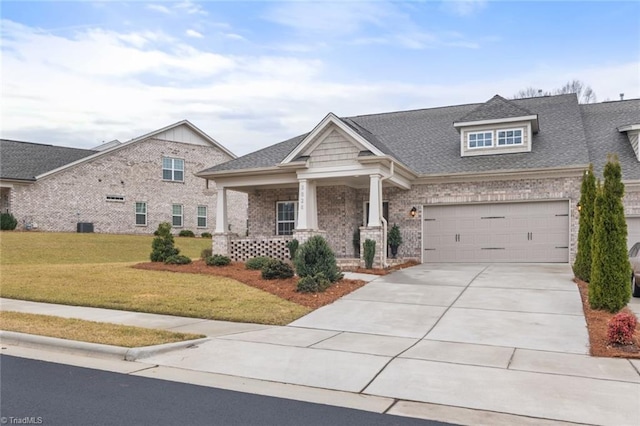 craftsman-style home featuring driveway, covered porch, a shingled roof, a front lawn, and brick siding