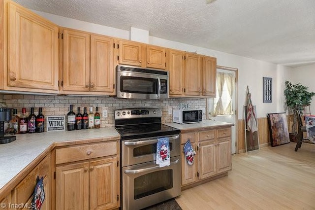 kitchen with light hardwood / wood-style flooring, backsplash, a textured ceiling, light brown cabinetry, and appliances with stainless steel finishes