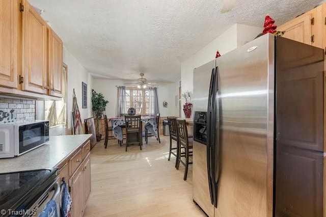 kitchen with a textured ceiling, ceiling fan, stainless steel refrigerator with ice dispenser, and light hardwood / wood-style flooring