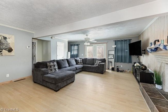 living room featuring a textured ceiling, ceiling fan, crown molding, a fireplace, and light hardwood / wood-style floors