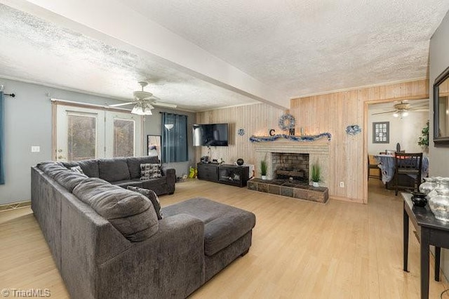 living room featuring beam ceiling, ceiling fan, wood walls, a textured ceiling, and light wood-type flooring