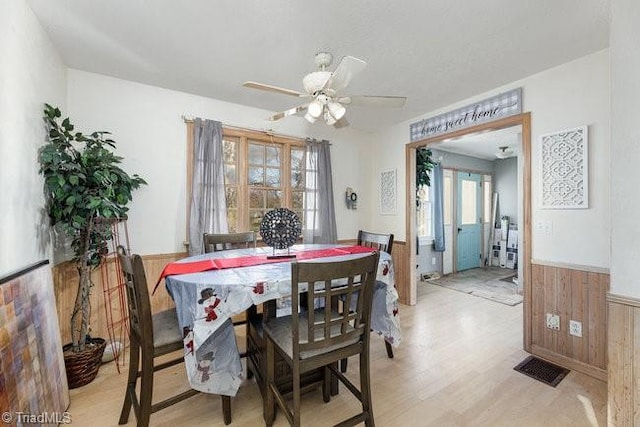 dining room with ceiling fan, wooden walls, and light hardwood / wood-style flooring