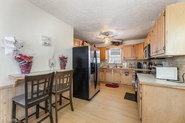 kitchen with backsplash, stainless steel appliances, ceiling fan, sink, and light hardwood / wood-style floors