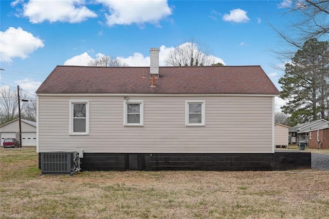 back of house with central air condition unit, a yard, roof with shingles, and a chimney