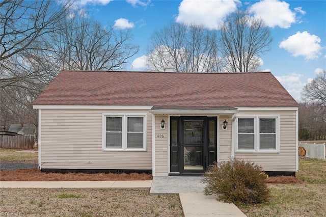 view of front of home with a front yard, roof with shingles, and fence