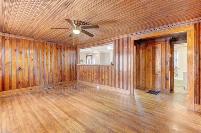 spare room featuring wooden walls, wood ceiling, wood finished floors, and a ceiling fan