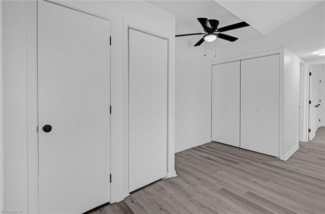 unfurnished bedroom with two closets, a ceiling fan, and wood finished floors