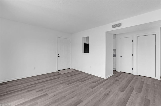 empty room with visible vents, a textured ceiling, baseboards, and wood finished floors