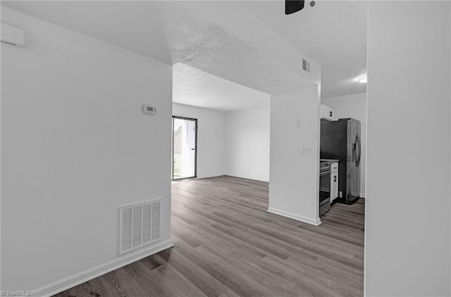 spare room with visible vents, a textured ceiling, baseboards, and wood finished floors