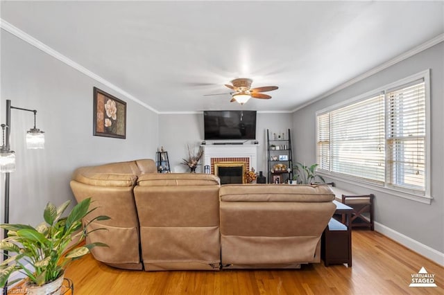 living room featuring ceiling fan, ornamental molding, a brick fireplace, and light wood-type flooring