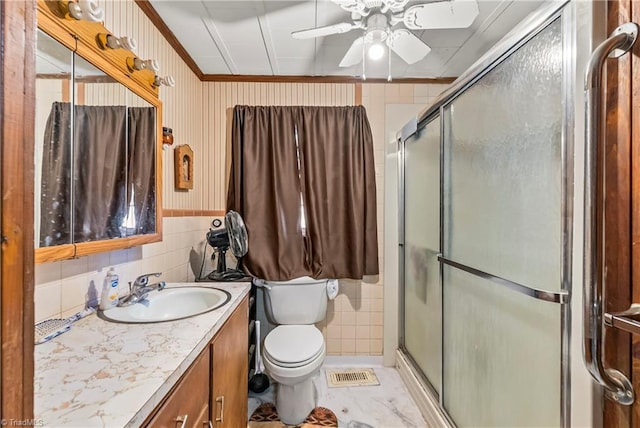 bathroom with tile walls, vanity, walk in shower, ceiling fan, and toilet