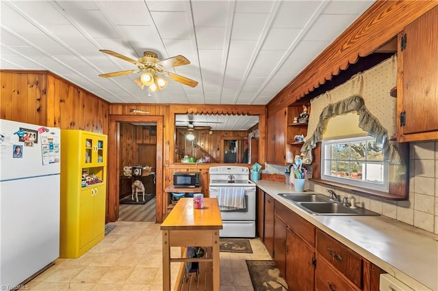 kitchen with sink, white appliances, ceiling fan, wooden walls, and decorative backsplash